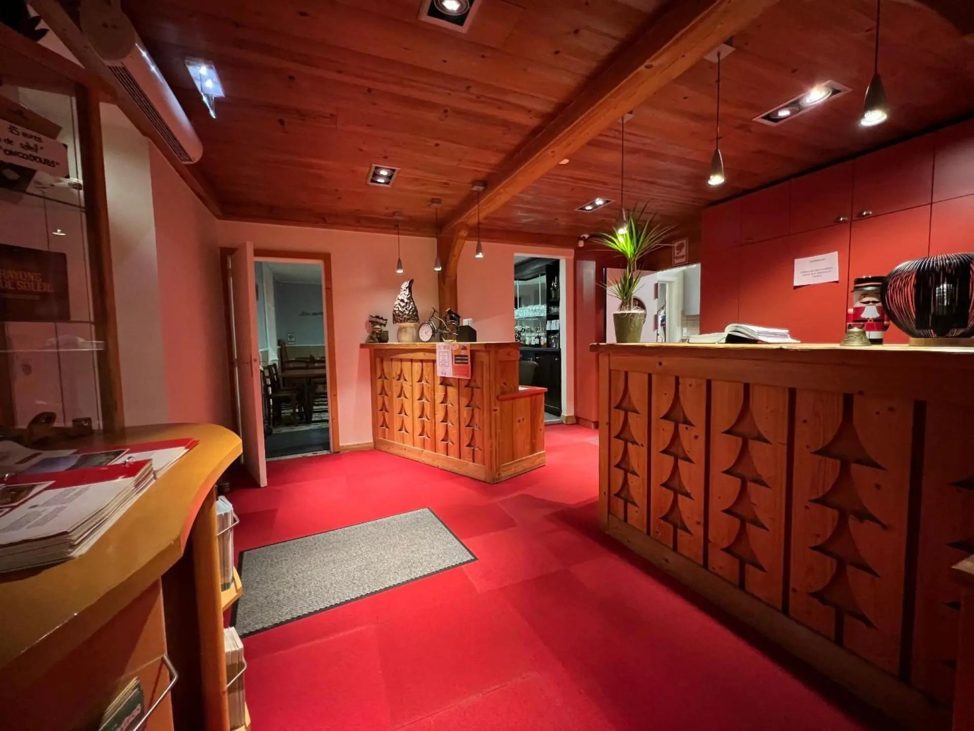 Hall d’accueil chaleureux avec moquette rouge, plafond en bois et comptoirs en bois ornés de sapins sculptés.