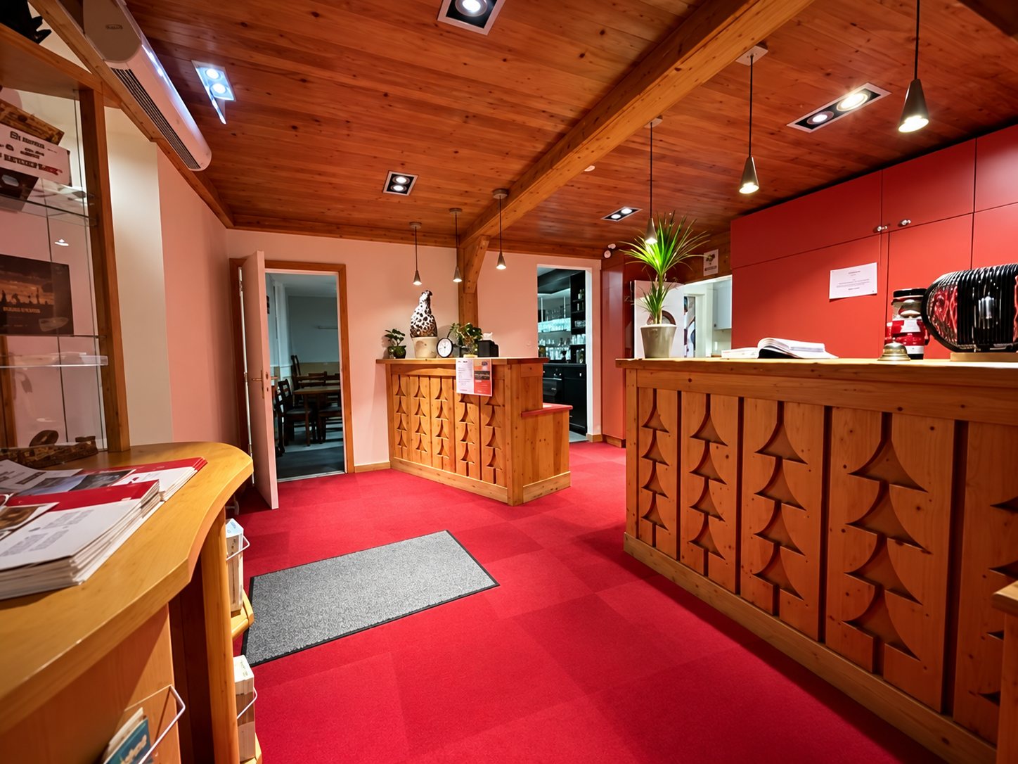 Hall de réception chaleureux avec moquette rouge, plafond en bois et comptoirs ornés de motifs de sapins sculptés.