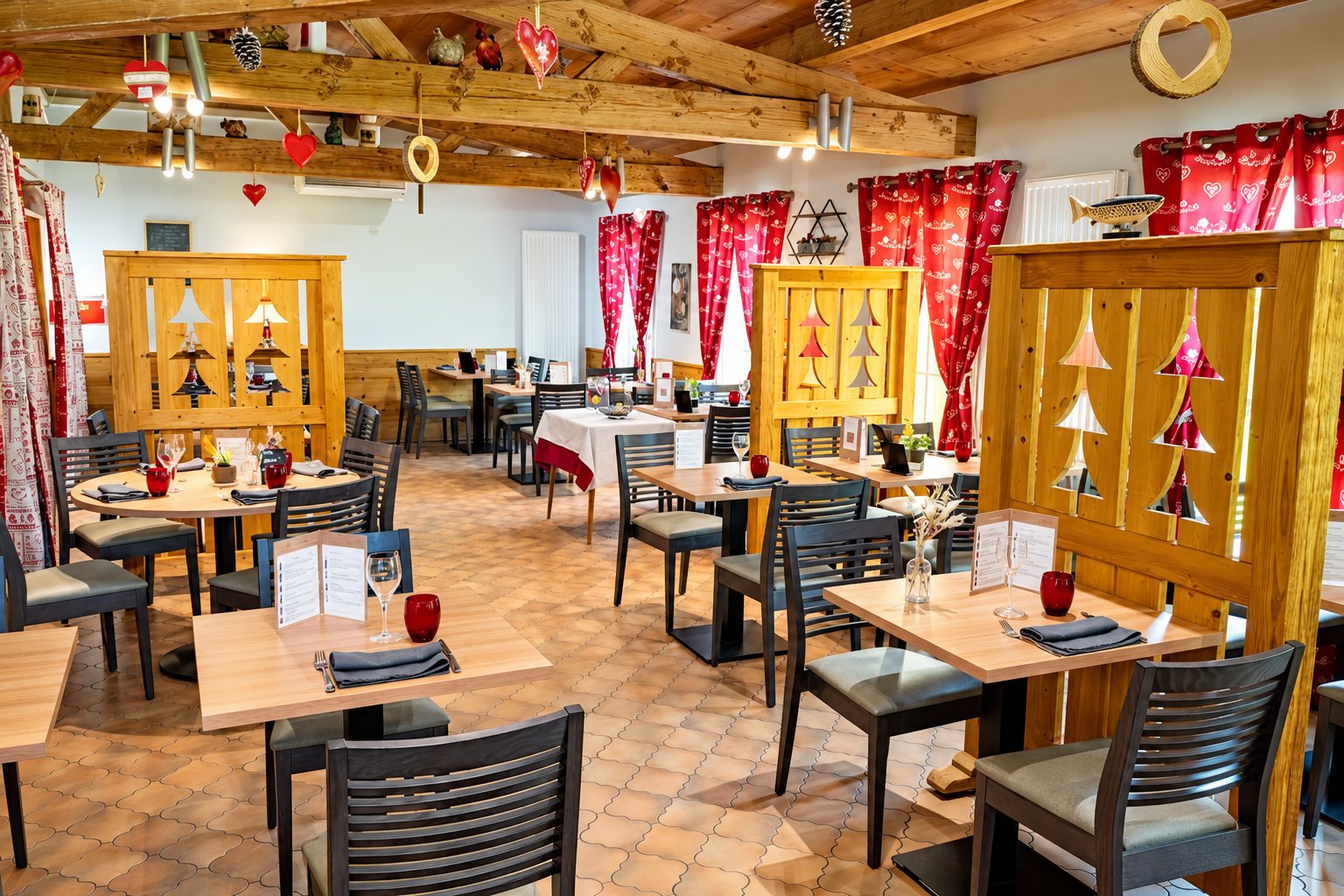 Salle de restaurant au style chalet avec poutres en bois, cloisons ajourées en sapin, rideaux rouges et tables dressées avec serviettes grises et verres rouges.