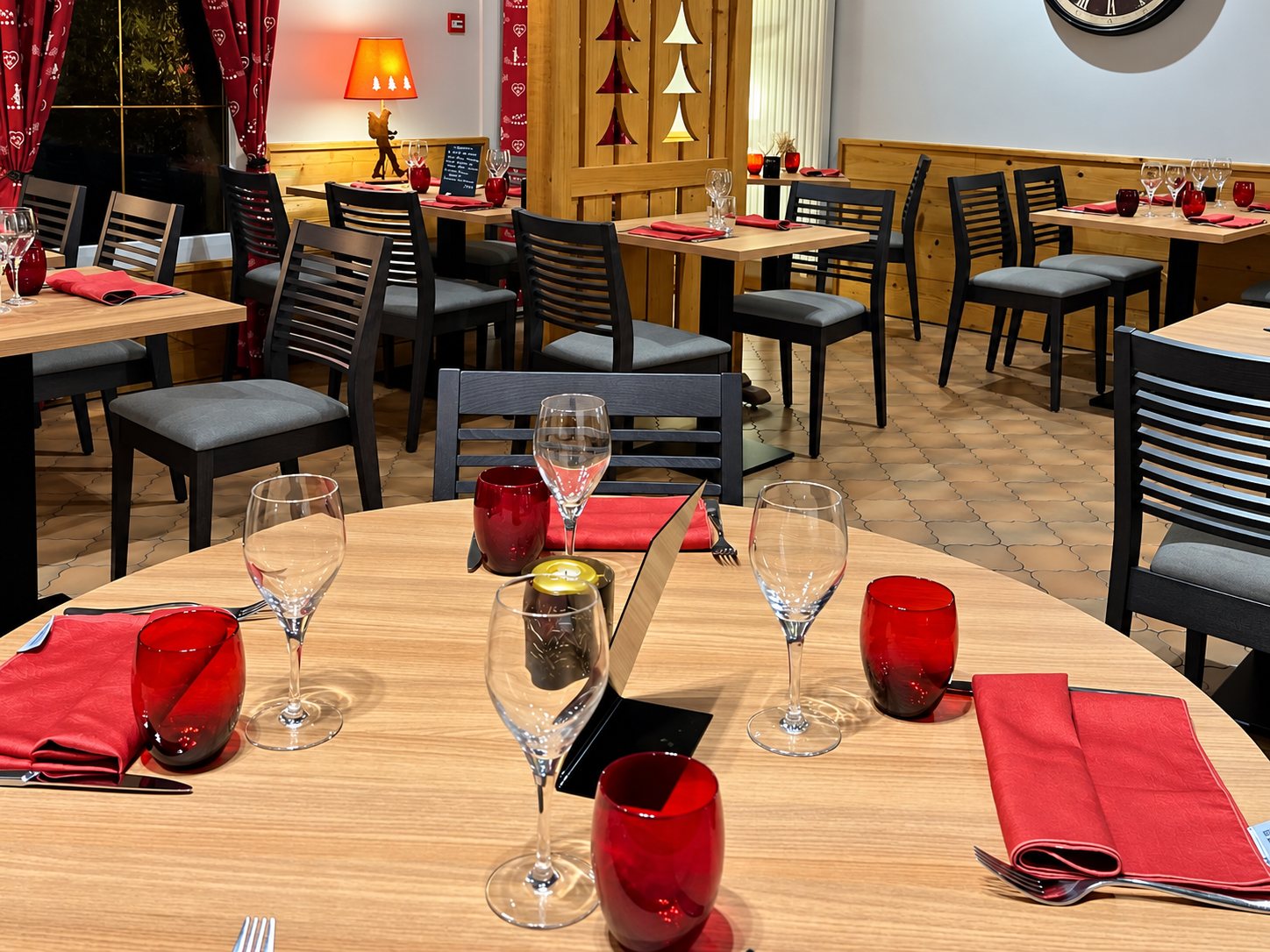 Salle de restaurant de style chalet avec tables en bois dressées de verres, gobelets rouges et serviettes rouges.