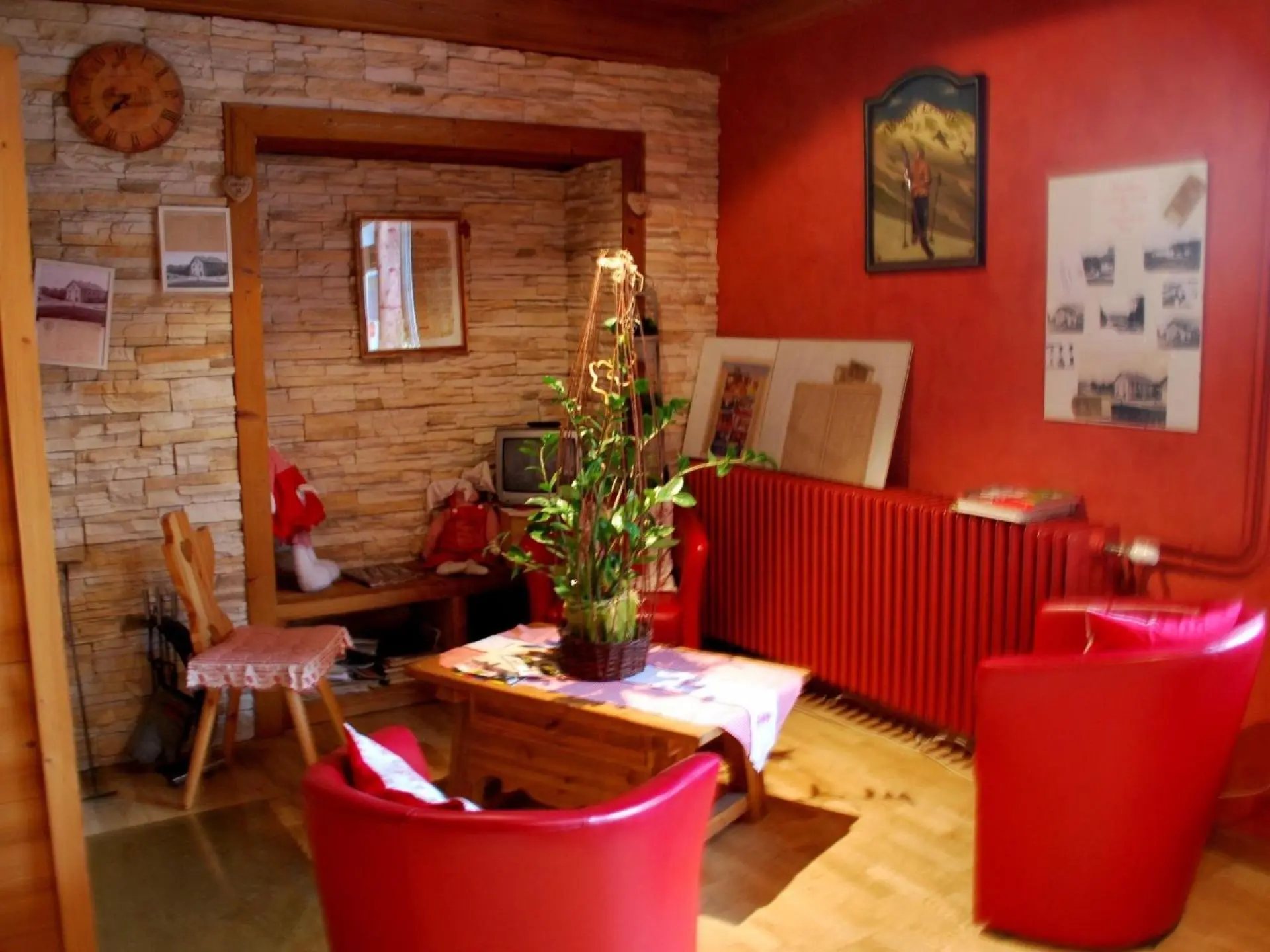 Un salon de style montagnard aux murs rouges, avec deux fauteuils rouges, une table en bois ornée d’une plante verte et un mur en pierres claires.